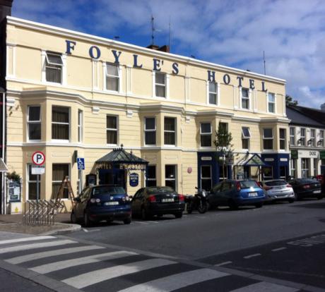 Cream-colored Foyle’s Hotel with ornate facade, parked cars, signs, and a zebra crossing.